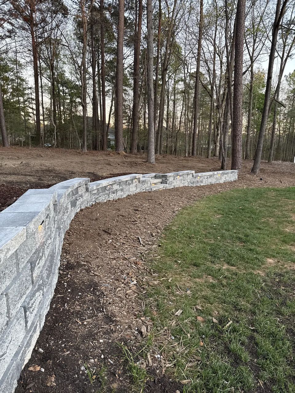 Curved block retaining wall sweeping through a wooded backyard