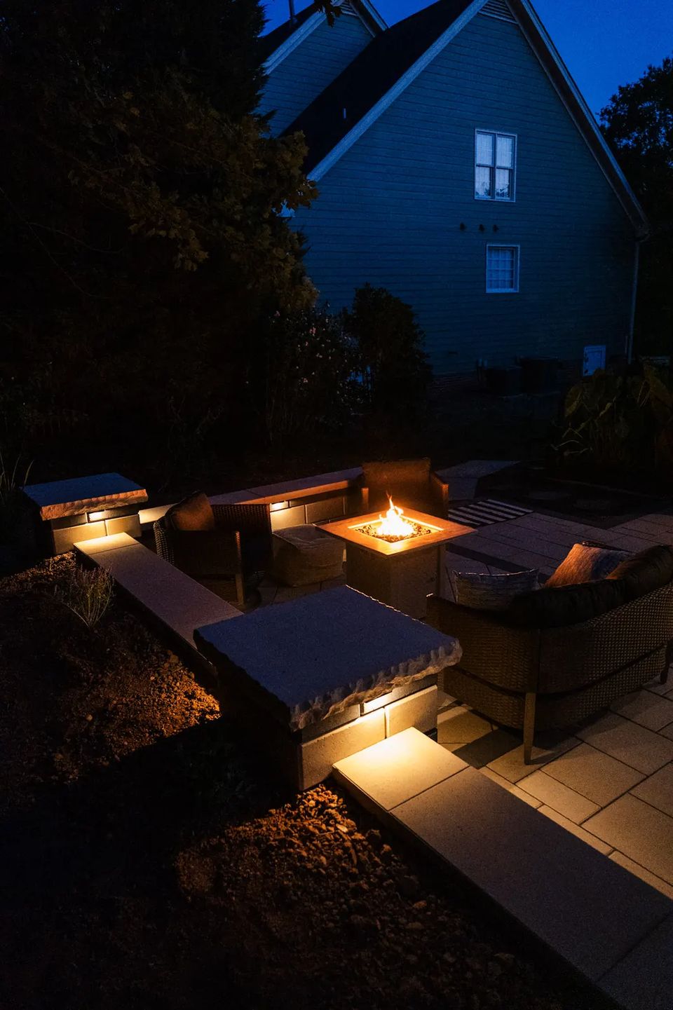 Fire table lounge at night with lit seat walls and steps down to the patio
