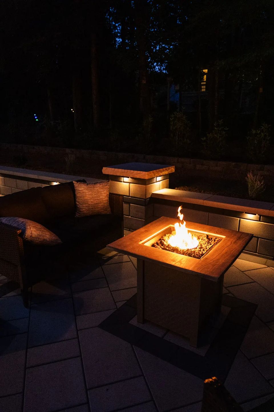 Fire table in front of a lit seat wall at night