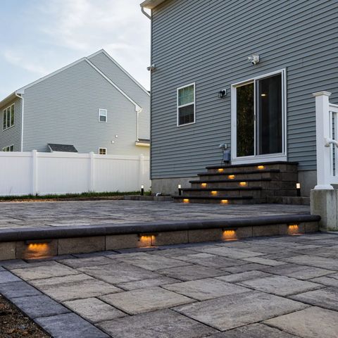 Lit steps down to a paver patio behind a blue gray house