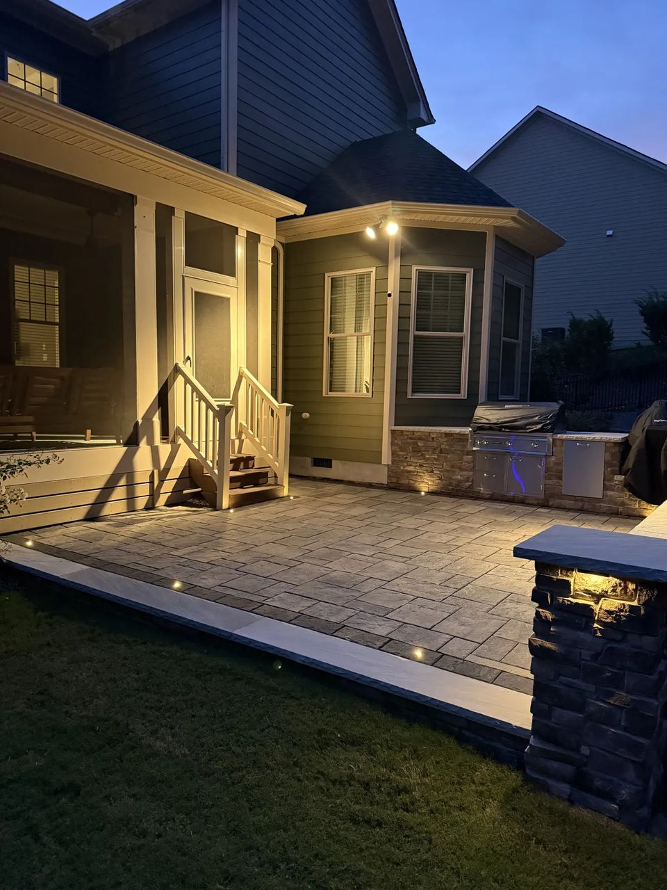 Wide dusk view of the lit kitchen patio and porch