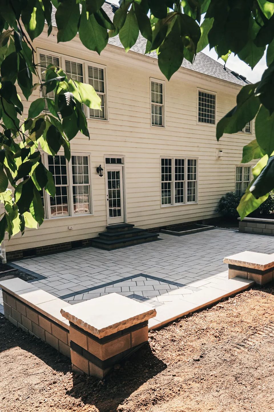 Slab patio with a contrasting square inlay and seat wall behind the house