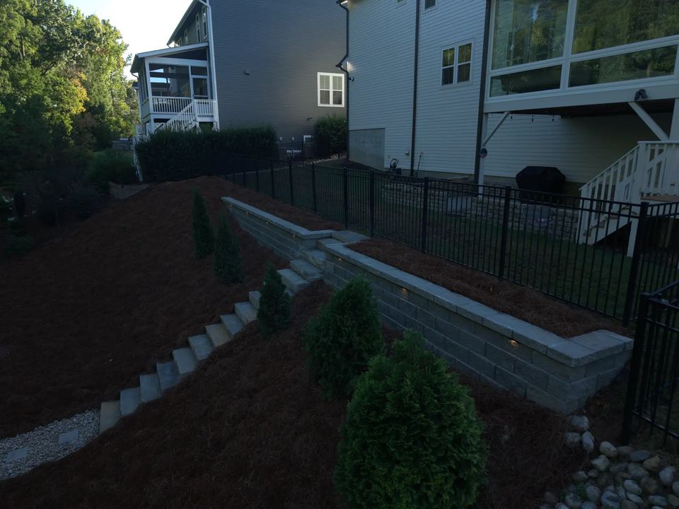 Retaining wall curving along the fence line with new plantings